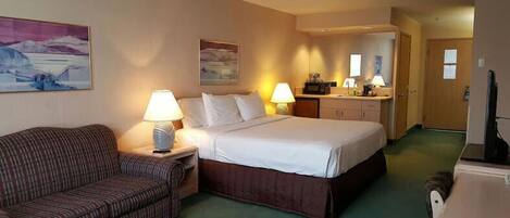 A hotel room with a bed, a sofa, a desk, and a kitchenette.