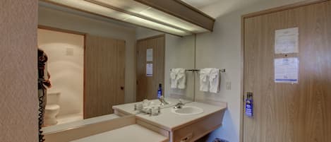 Ett hotellbadrum med en träinredd tvättställsmöbel, en stor spegel, ett handfat och en toalett.