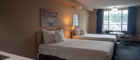 A hotel room with two beds, a desk, a chair, and a window with a view of the outside.