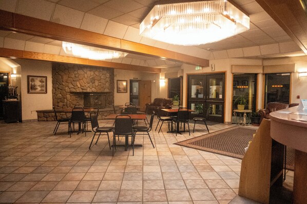 A spacious indoor area with multiple tables and chairs, a stone wall, and a large chandelier.