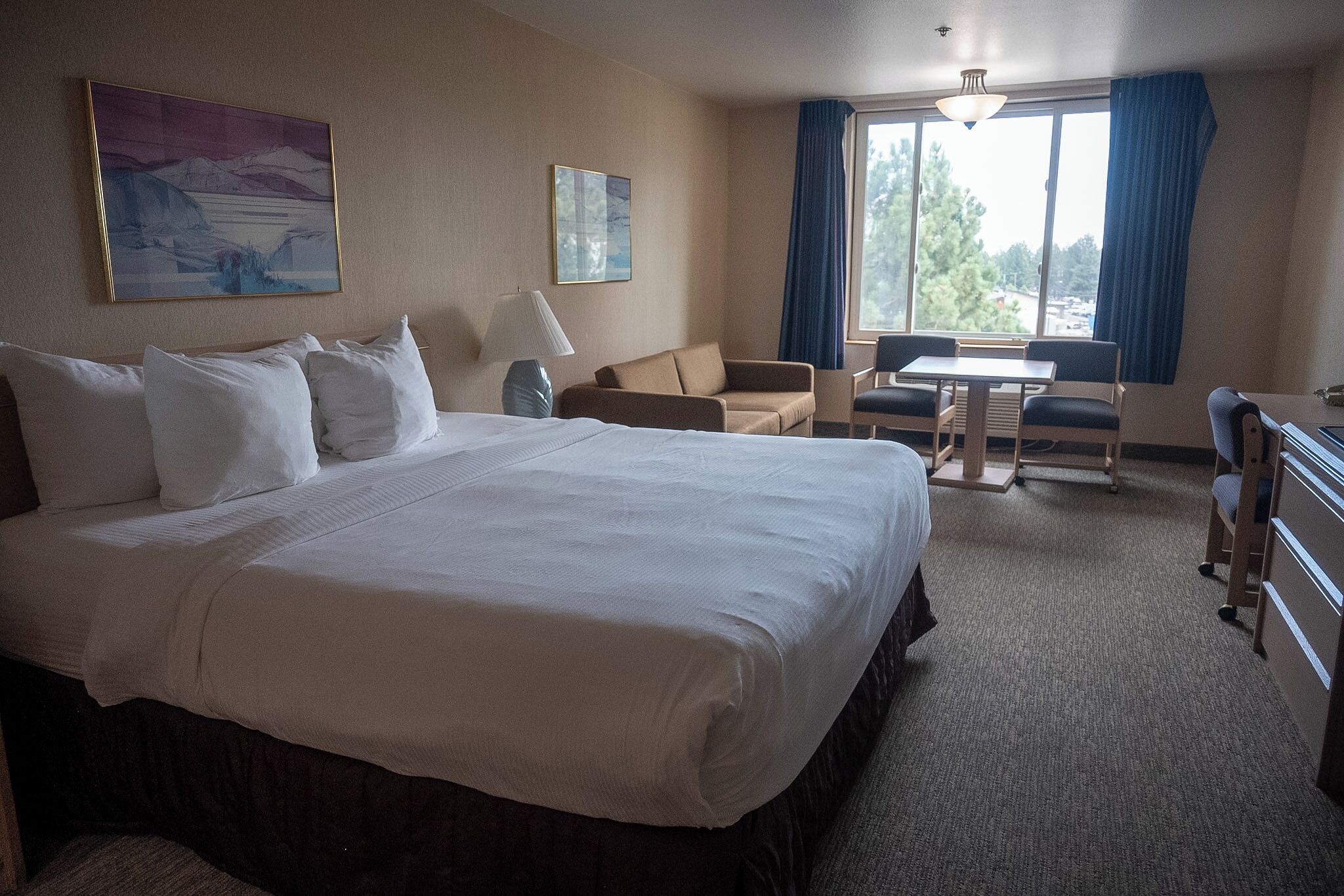 A hotel room with a large bed, a desk, a chair, and a window with curtains.
