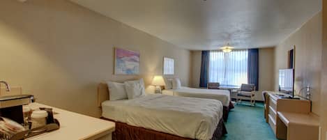 A hotel room with two beds, a desk, a chair, a TV, and a window with curtains.