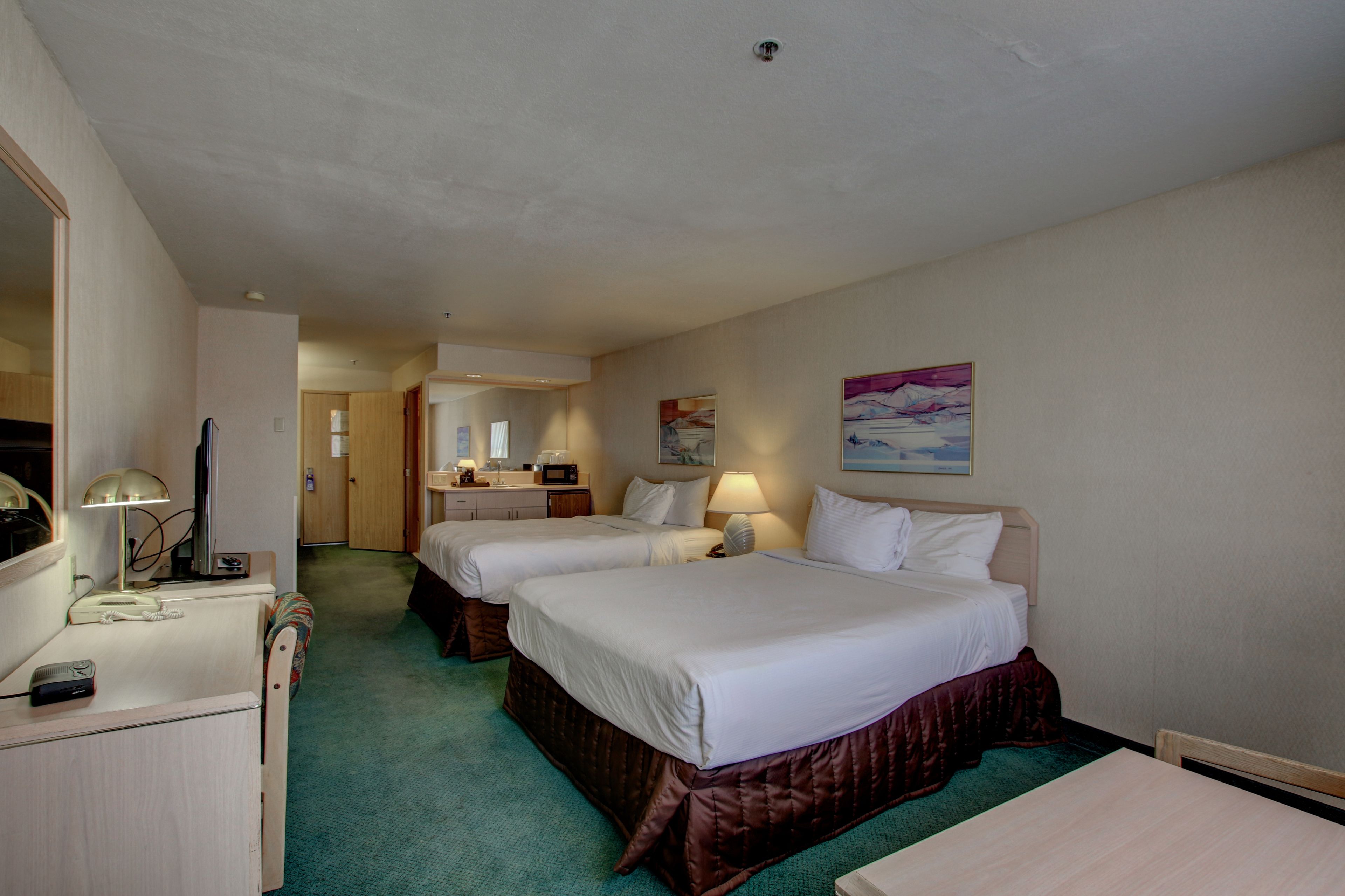 A hotel room with two beds, a desk, a chair, a mirror, and a painting on the wall.