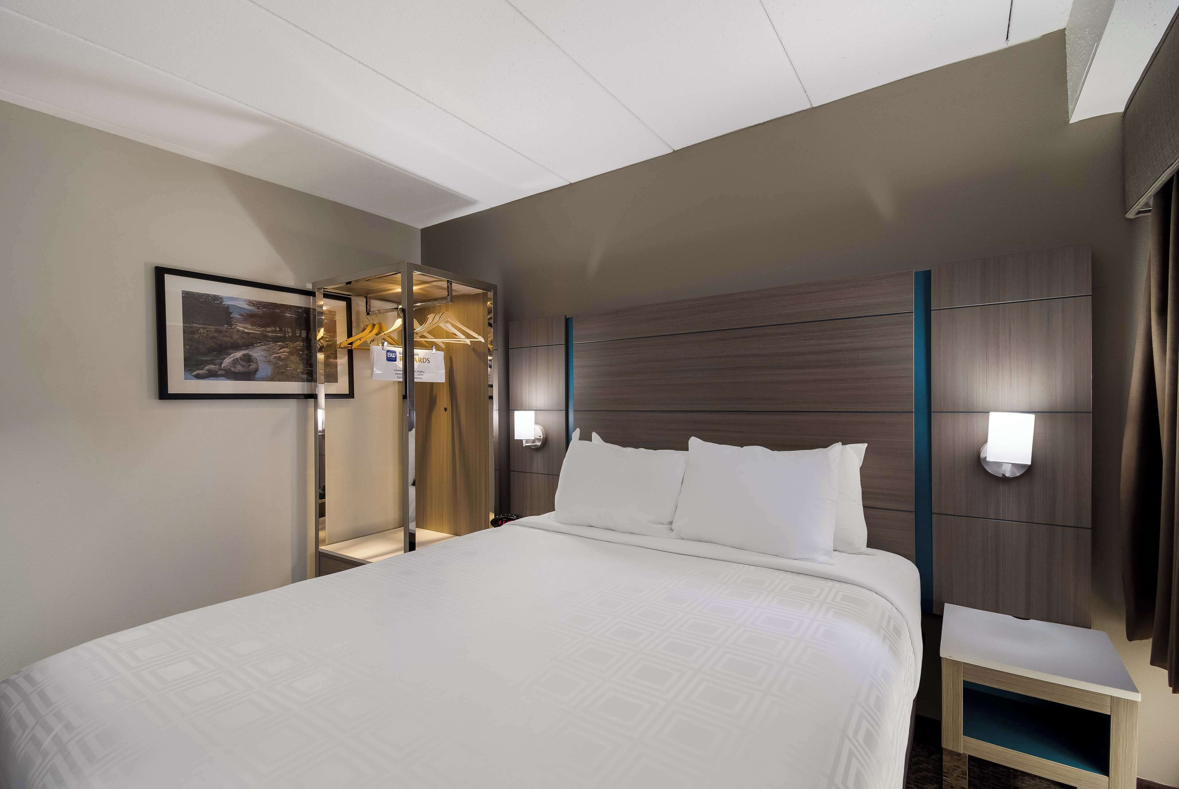A hotel room with a large bed, a nightstand, a wall-mounted light, and a framed picture on the wall.