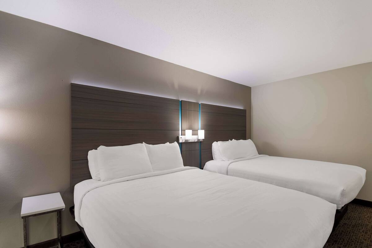 A hotel room with two beds, a nightstand, and a wall-mounted light fixture.