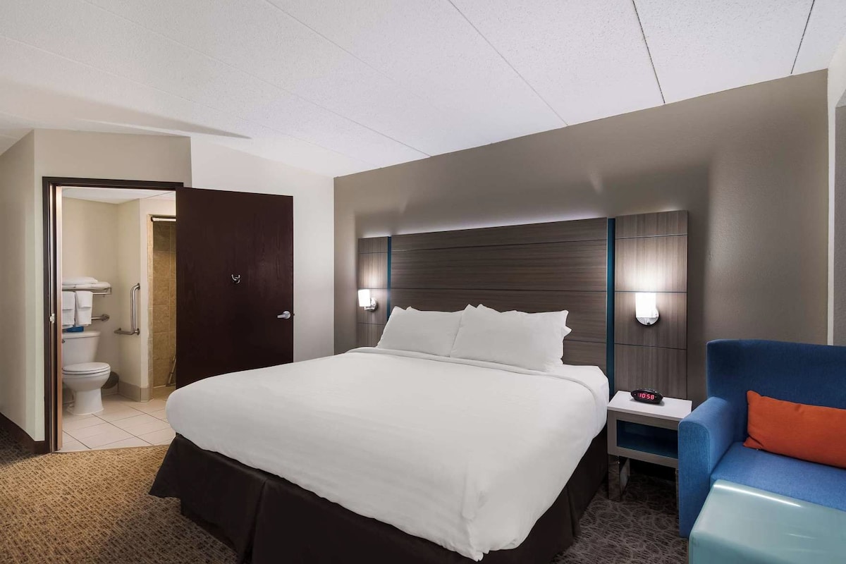 A hotel room with a large bed, bedside table, and a chair.