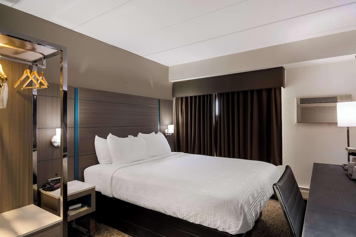 A hotel room with a large bed, a bedside table, a wardrobe, and a desk with a chair.
