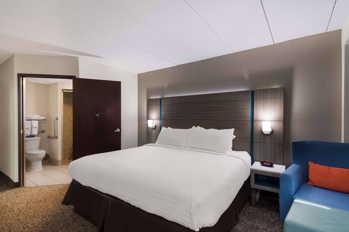 A hotel room with a large bed, bedside tables, a blue armchair, and a visible bathroom.