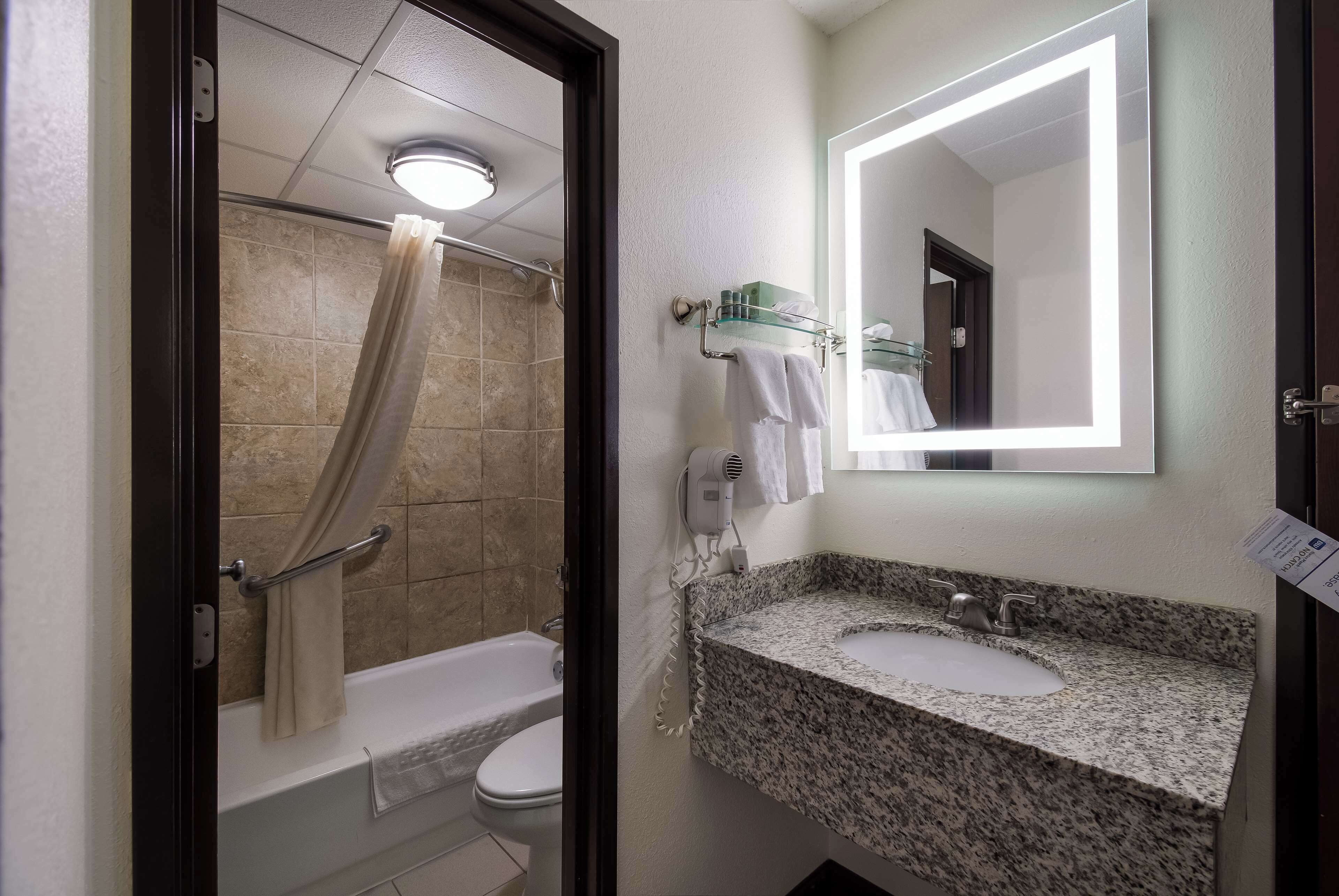A bathroom with a shower, toilet, sink, and a mirror with a light.