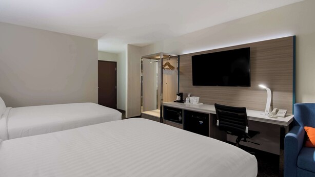 Ein Hotelzimmer mit zwei Betten, einem Schreibtisch mit Stuhl, einem Flachbildfernseher und einem Spiegel.