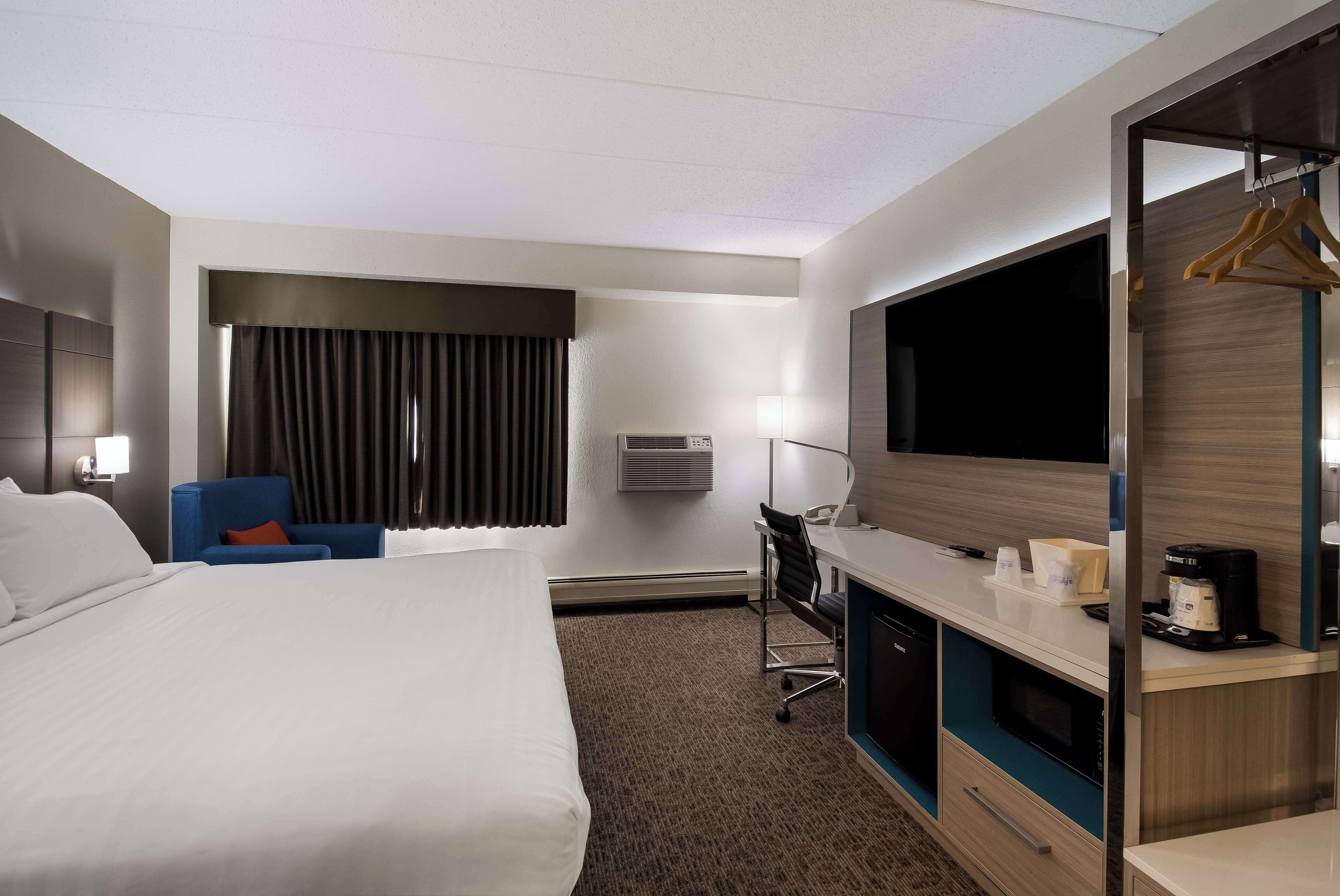 A hotel room with a large bed, a desk with a chair, a television, and a wardrobe.