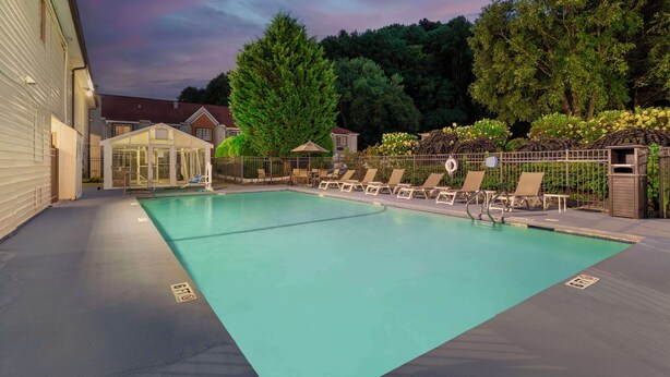 A swimming pool with lounge chairs and a covered seating area, surrounded by trees and a fence. - Best Western Mountainbrook Inn (Maggie Valley)