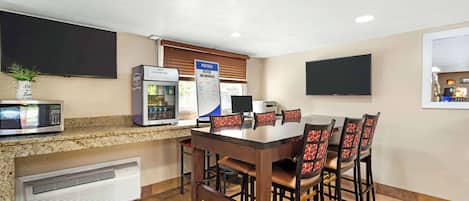 A dining area with a table and chairs, a microwave, a coffee machine, and a menu board.