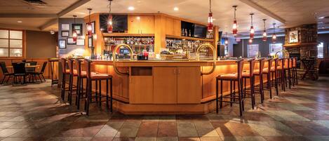 A bar area with a central counter, multiple stools, and a tiled floor.