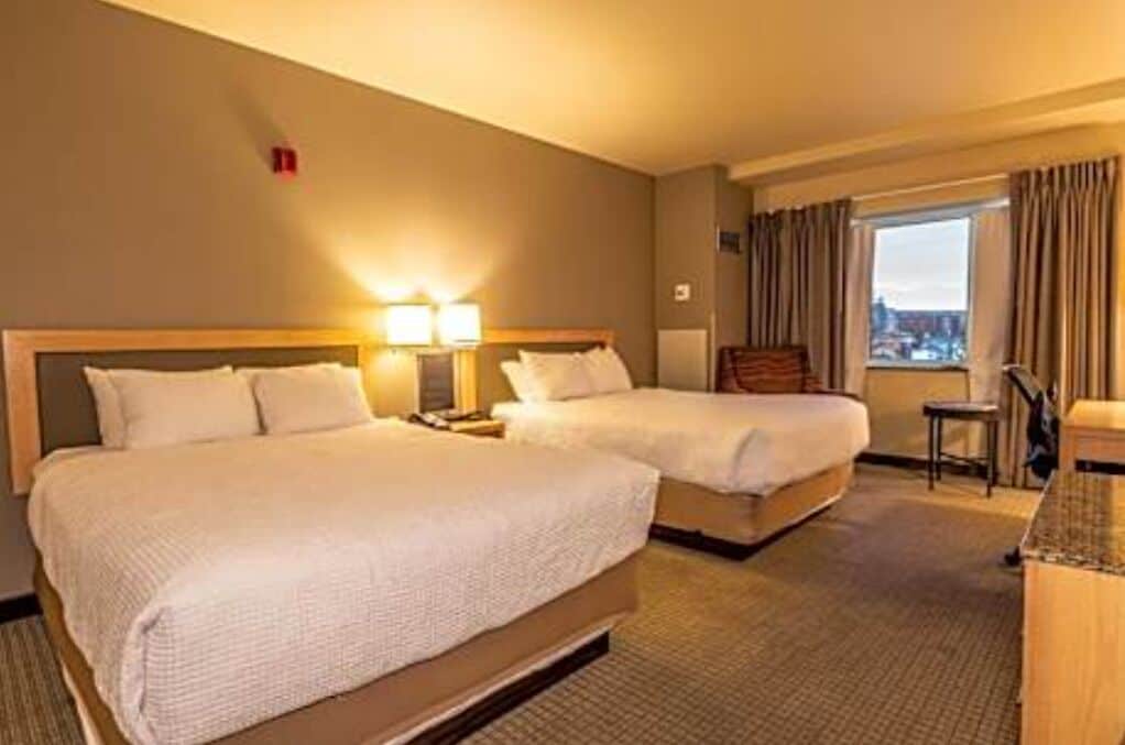 A hotel room with two beds, a desk, a chair, and a window with curtains.