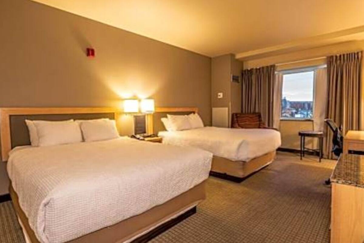 Une chambre d’hôtel avec deux lits, un bureau, une chaise et une fenêtre avec des rideaux.