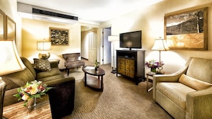 A hotel room with a sofa, armchair, coffee table, TV, and a painting on the wall.