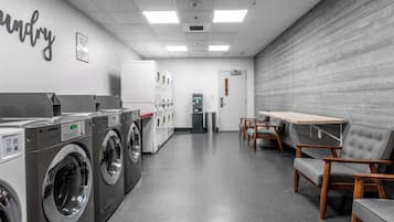 Une laverie équipée de plusieurs machines à laver, d’un espace de séchage et d’un coin salon avec des tables et des chaises.
