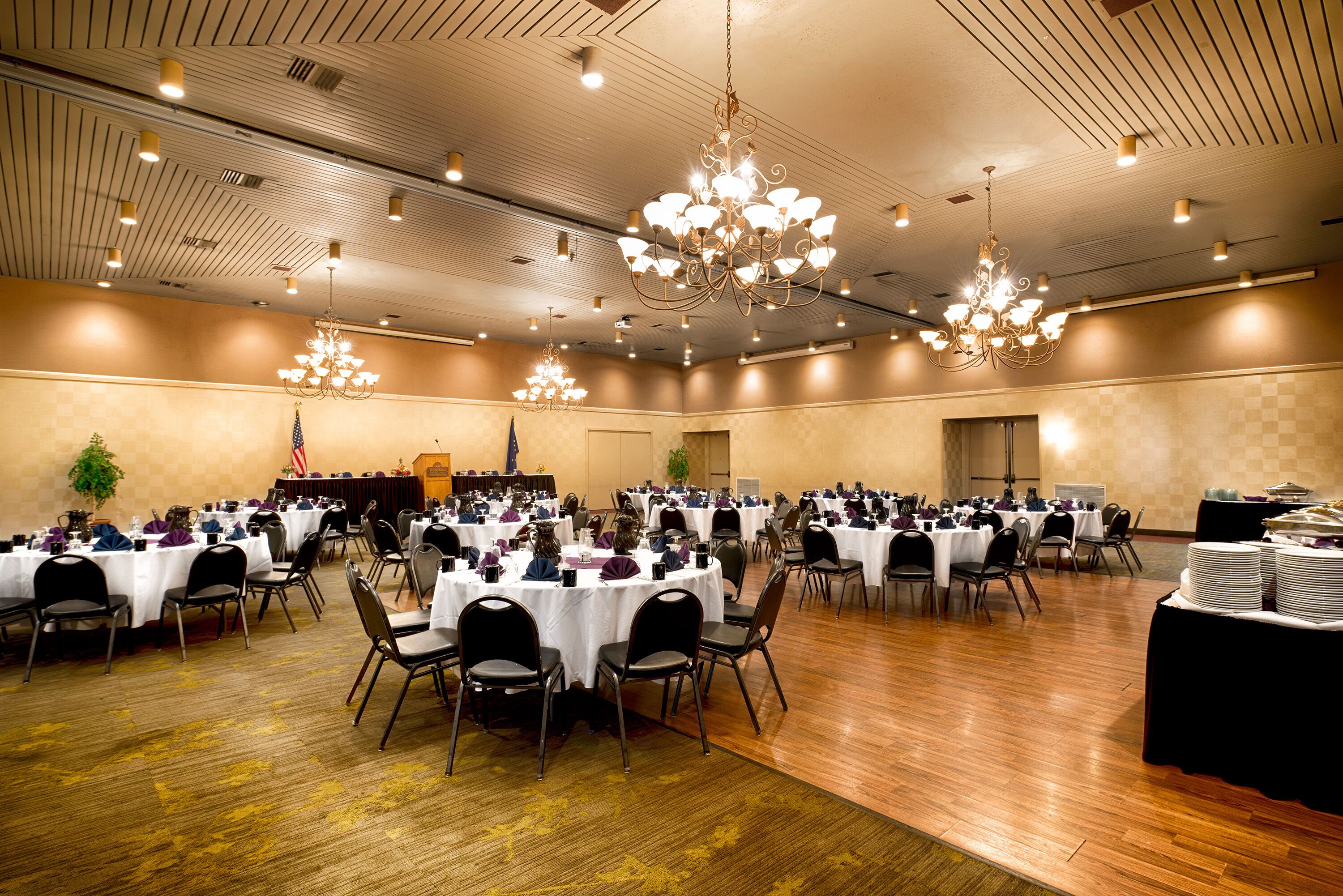 Une salle de banquet avec des tables rondes, des chaises, des lustres et une scène sur laquelle flotte un drapeau américain.