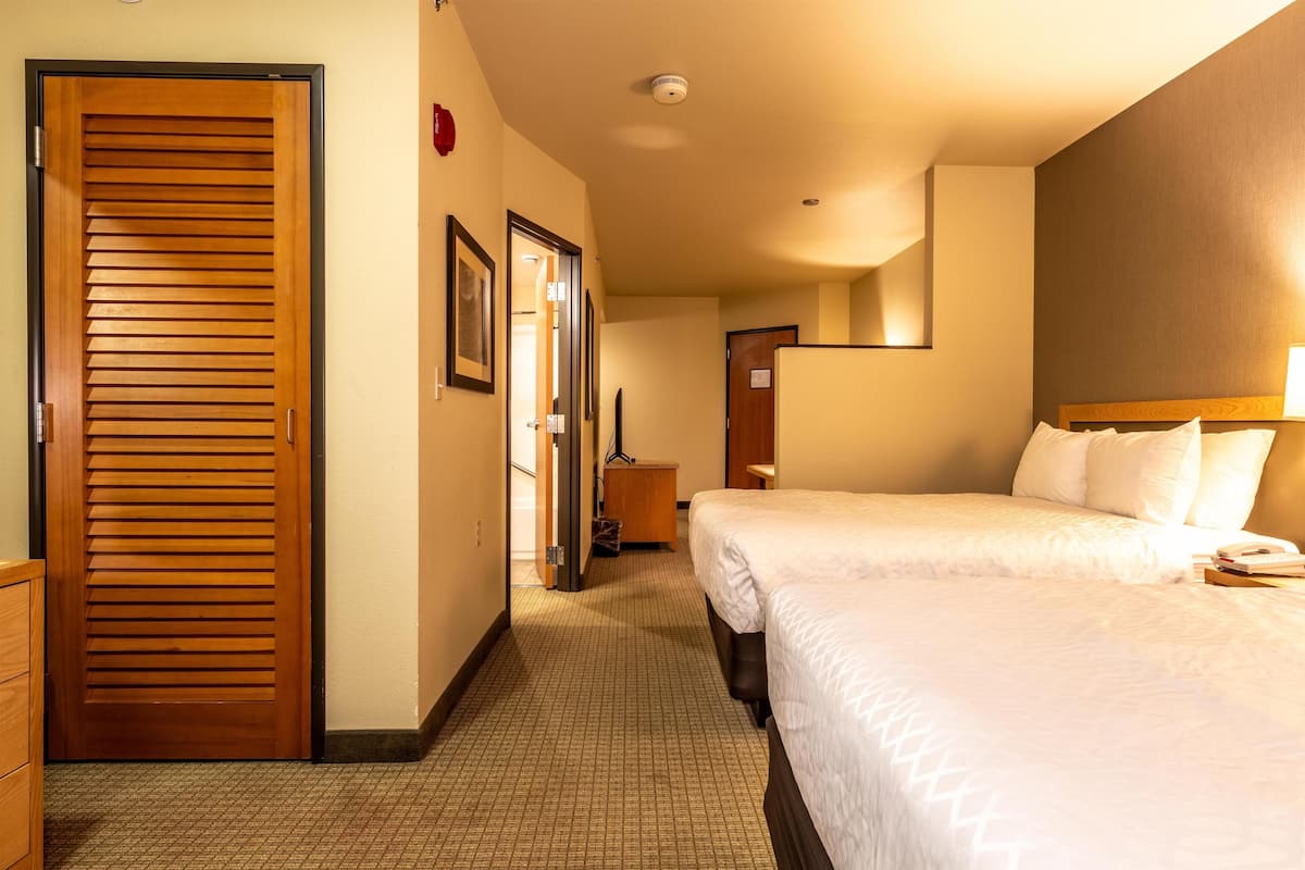 Une chambre d’hôtel avec deux lits, une porte en bois, un petit bureau et un miroir au mur.