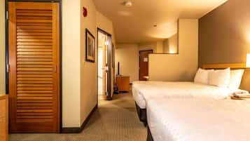 A hotel room with two beds, a wooden door, a small desk, and a mirror on the wall.