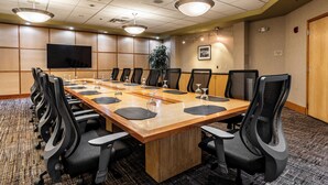 A conference room with a long wooden table, black chairs, and a flat-screen TV on the wall.