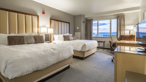 A hotel room with two beds, a desk, a chair, and a view of the city.
