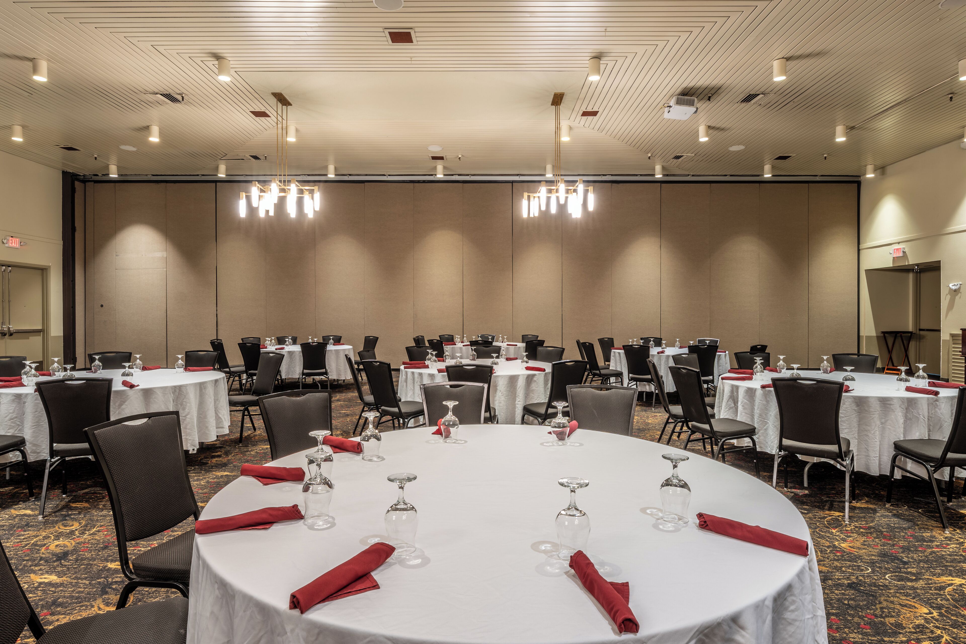 En festlokal med runda bord uppdukade för middag, utrustad med stolar, bord och glasvaror.