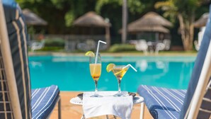 Escena junto a la piscina con dos sillones de descanso y una mesa con dos bebidas.