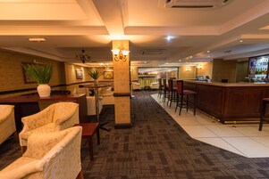 Vestíbulo de hotel con recepción, zona de bar, asientos y elementos decorativos.