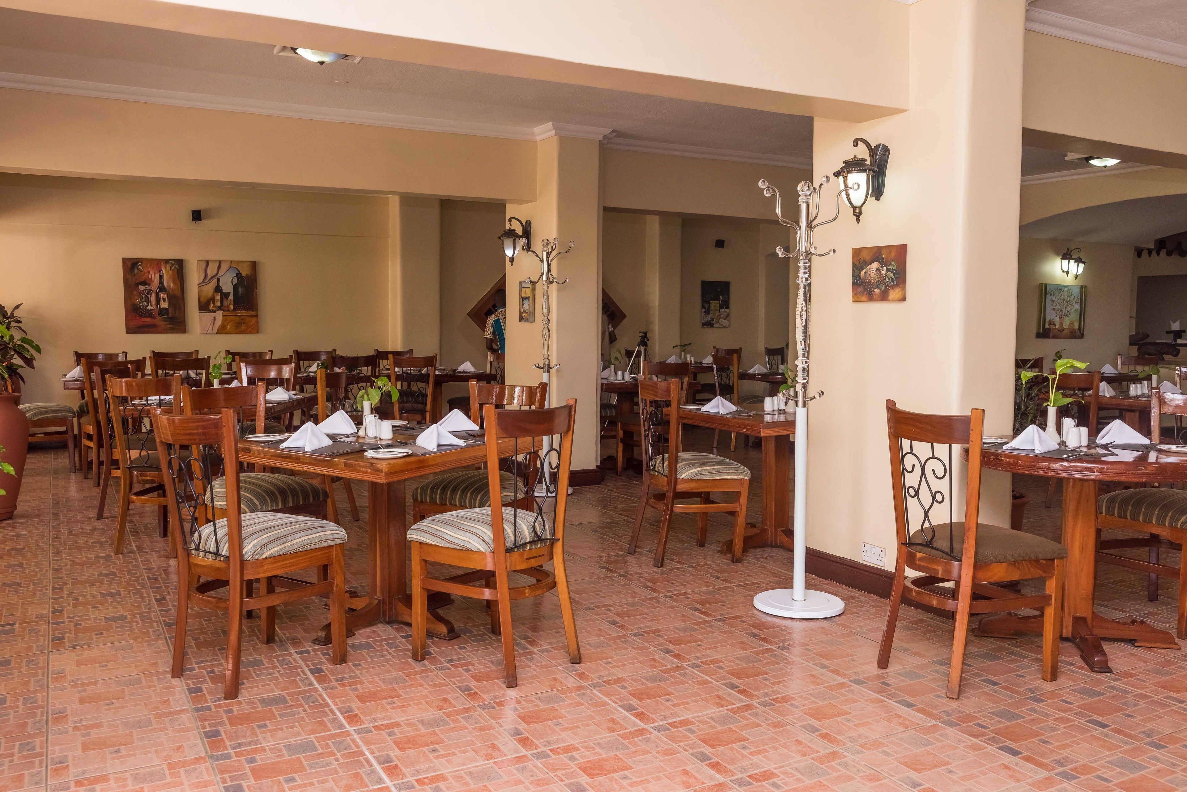 Un área de comedor con varias mesas y sillas de madera, dispuestas en un espacio amplio.