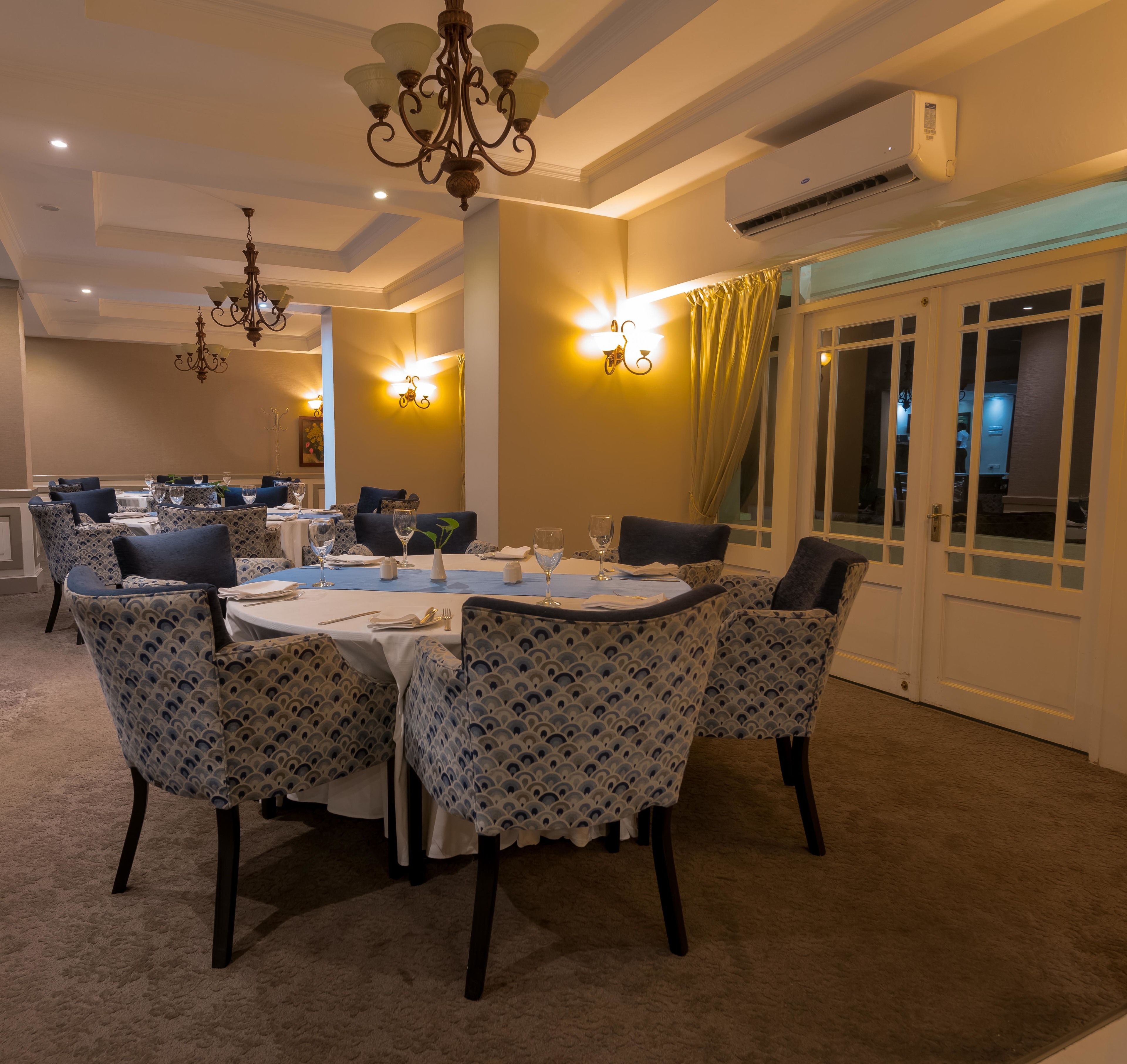 A dining area with round tables, patterned chairs, chandeliers, and wall sconces.