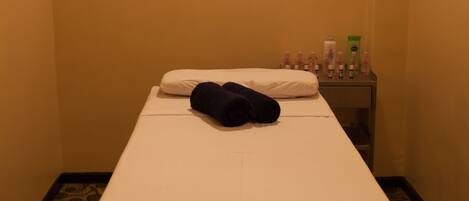 A small, narrow room with a single bed, a nightstand with toiletries, and patterned floor tiles.