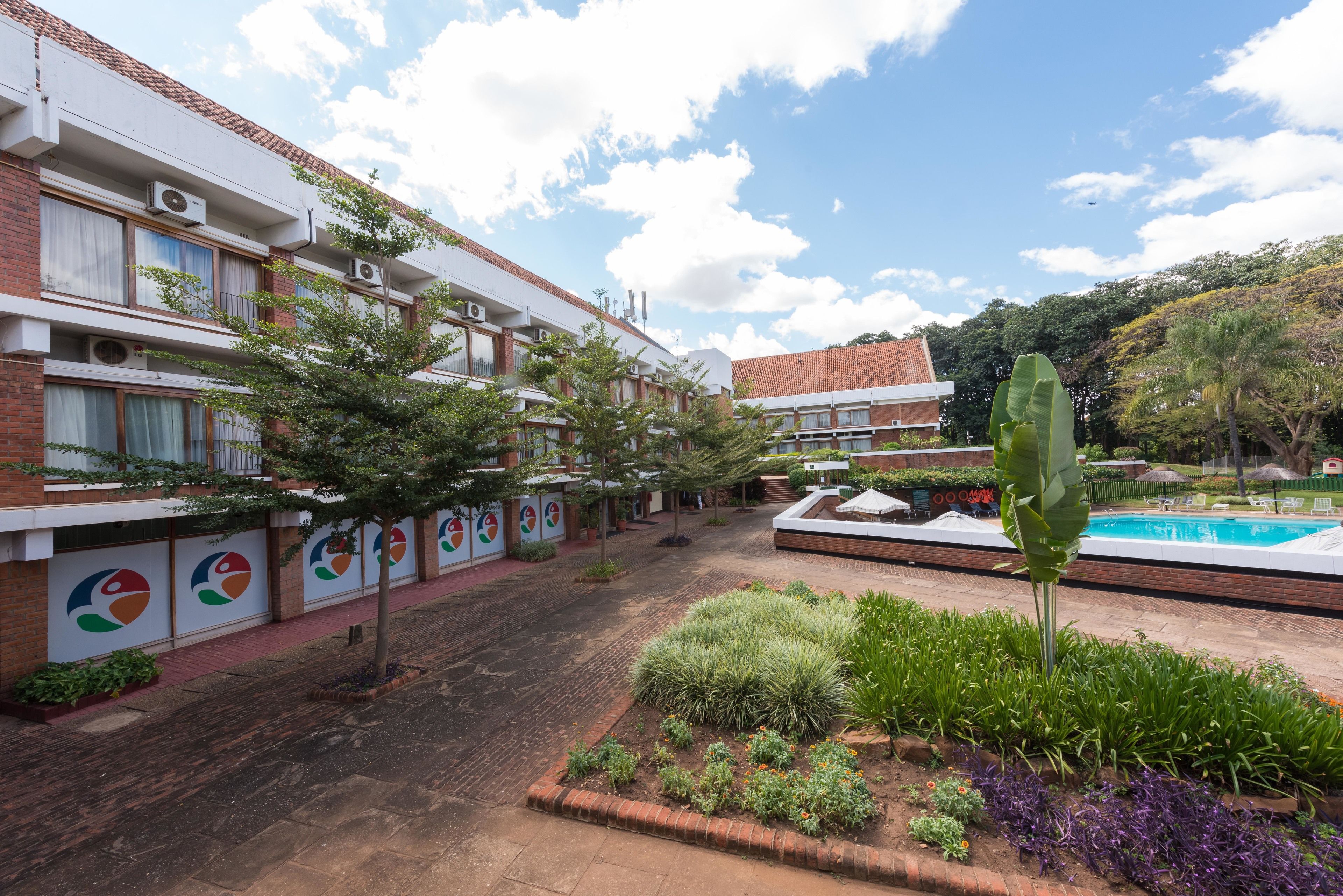 A courtyard with a swimming pool, surrounded by multi-story buildings with air conditioning units, and a variety of plants and shrubs.