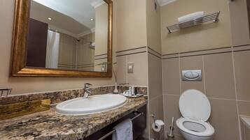 Un baño con encimera de granito, un lavabo blanco, un espejo, un inodoro y un perchero para toallas.