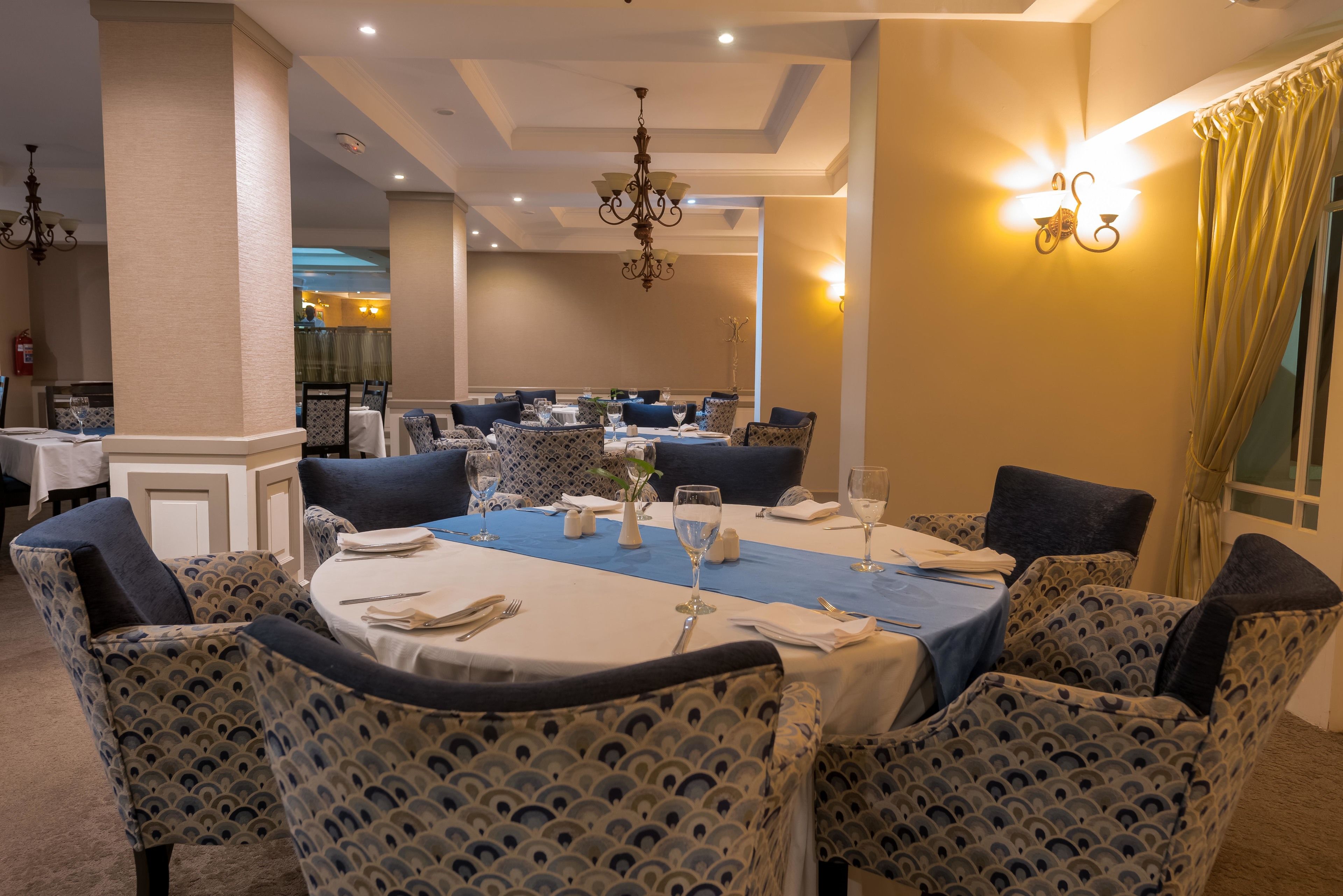 Un espace repas avec des tables rondes, des nappes bleues et des chaises à motifs.