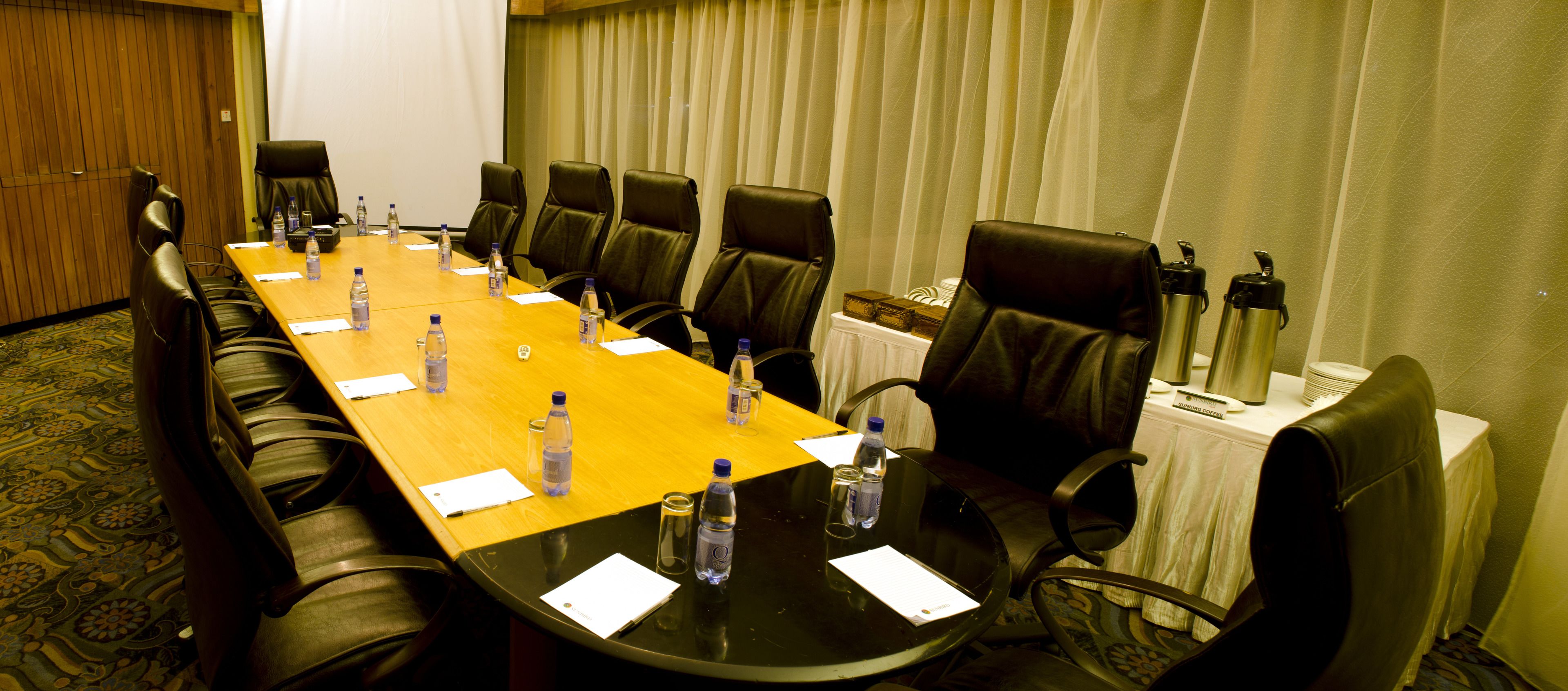 A conference room with a long table, chairs, water bottles, and a coffee machine.