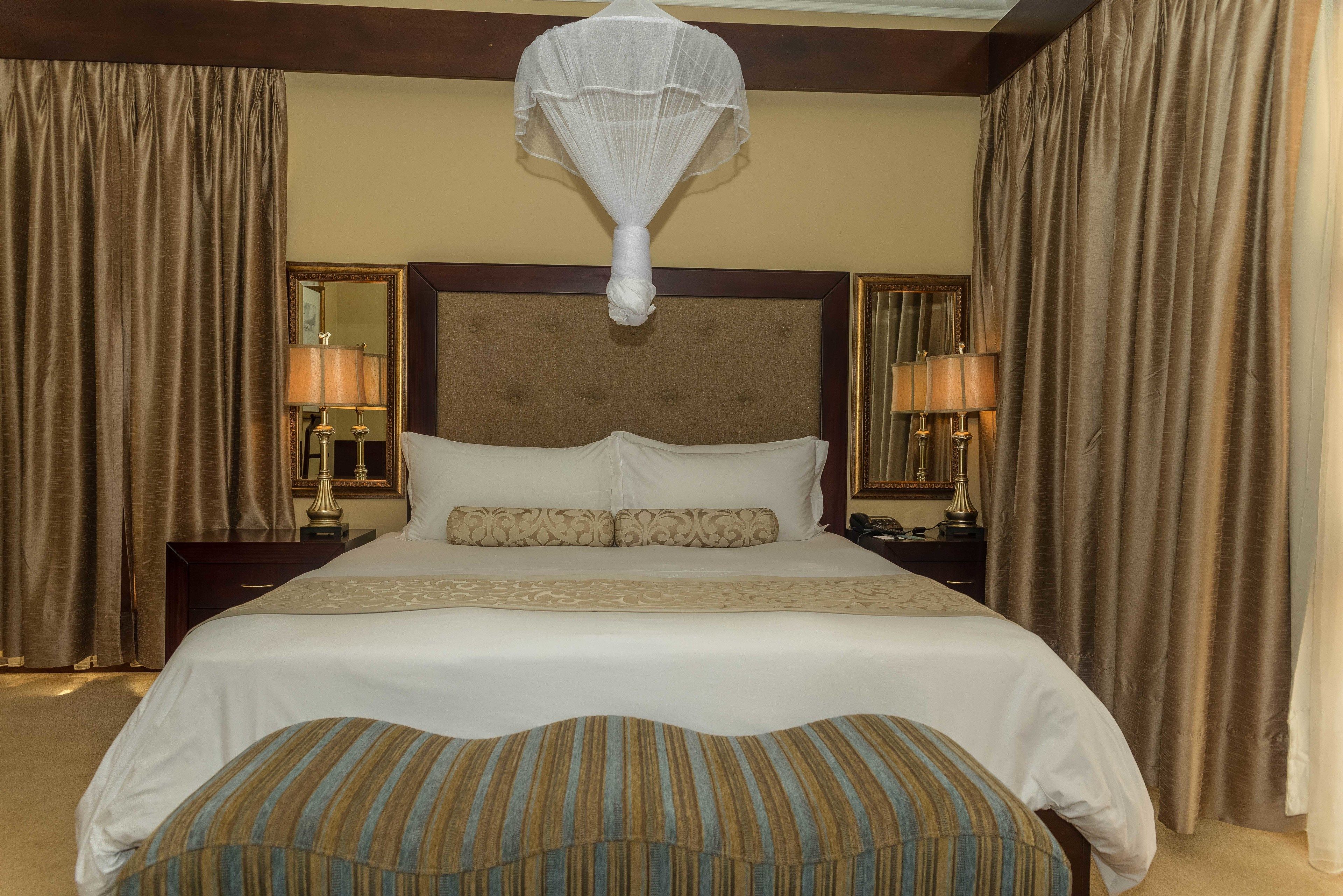 Une chambre d’hôtel avec un grand lit, deux tables de chevet avec des lampes, un lit à baldaquin et des rideaux.
