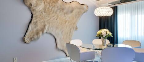 Un comedor moderno con una mesa de vidrio, sillas blancas y un trozo de piel de animal colgado en la pared.