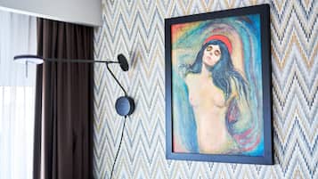 Uma obra de arte emoldurada em uma parede com padrão geométrico, um abajur e uma janela com cortinas.