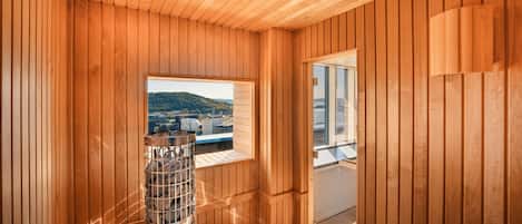 A wooden interior with a sauna, a window with a view of buildings, and a door leading to an outdoor area.