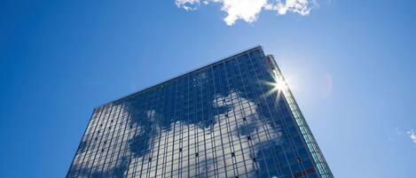 Un edificio alto de vidrio con cielo despejado y nubes al fondo.