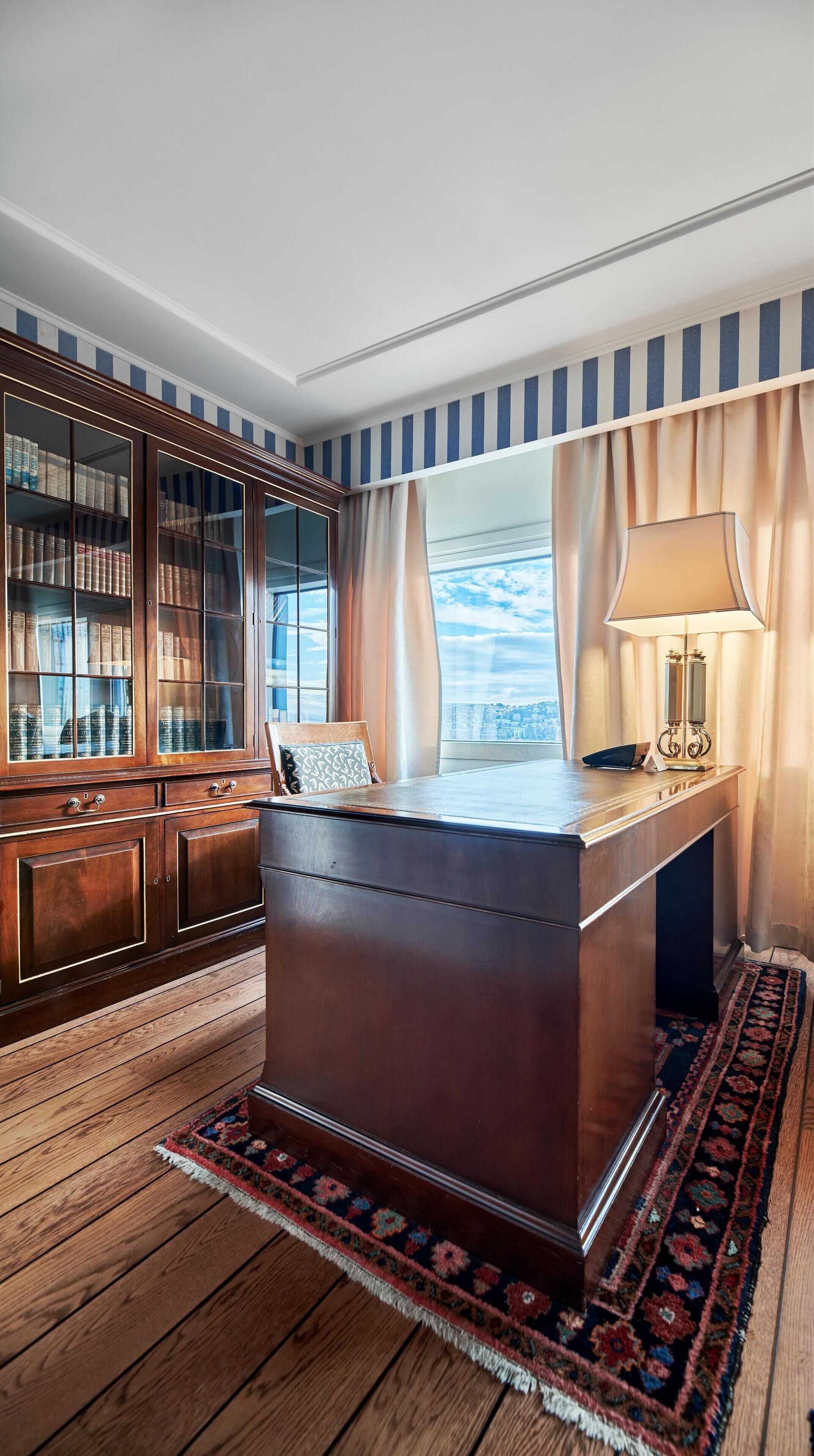Ein Arbeitszimmer mit großem Schreibtisch, Bücherregalen und Blick auf die Stadt.