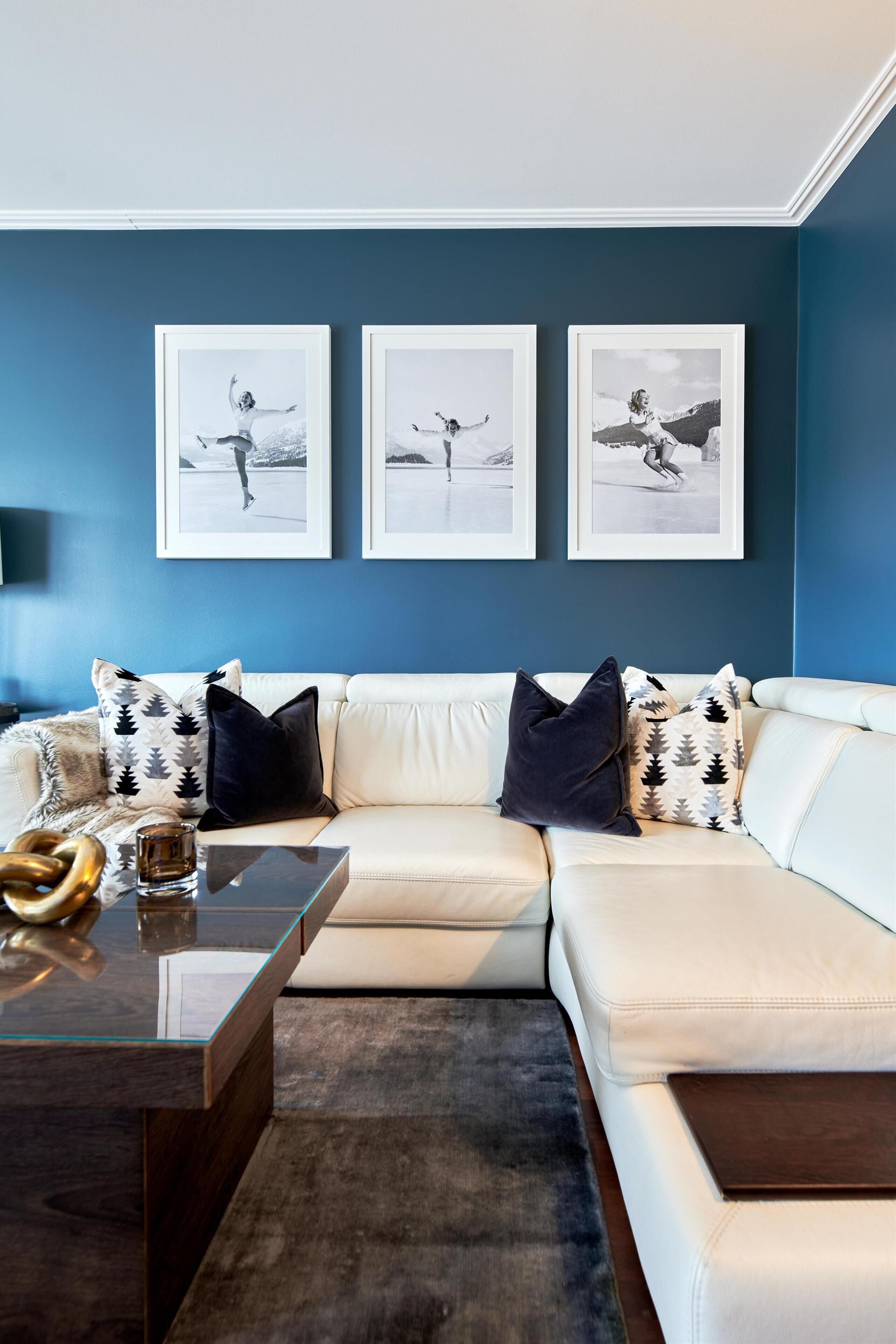 A modern living room with a white leather sofa, a glass coffee table, and three framed photographs on the wall.