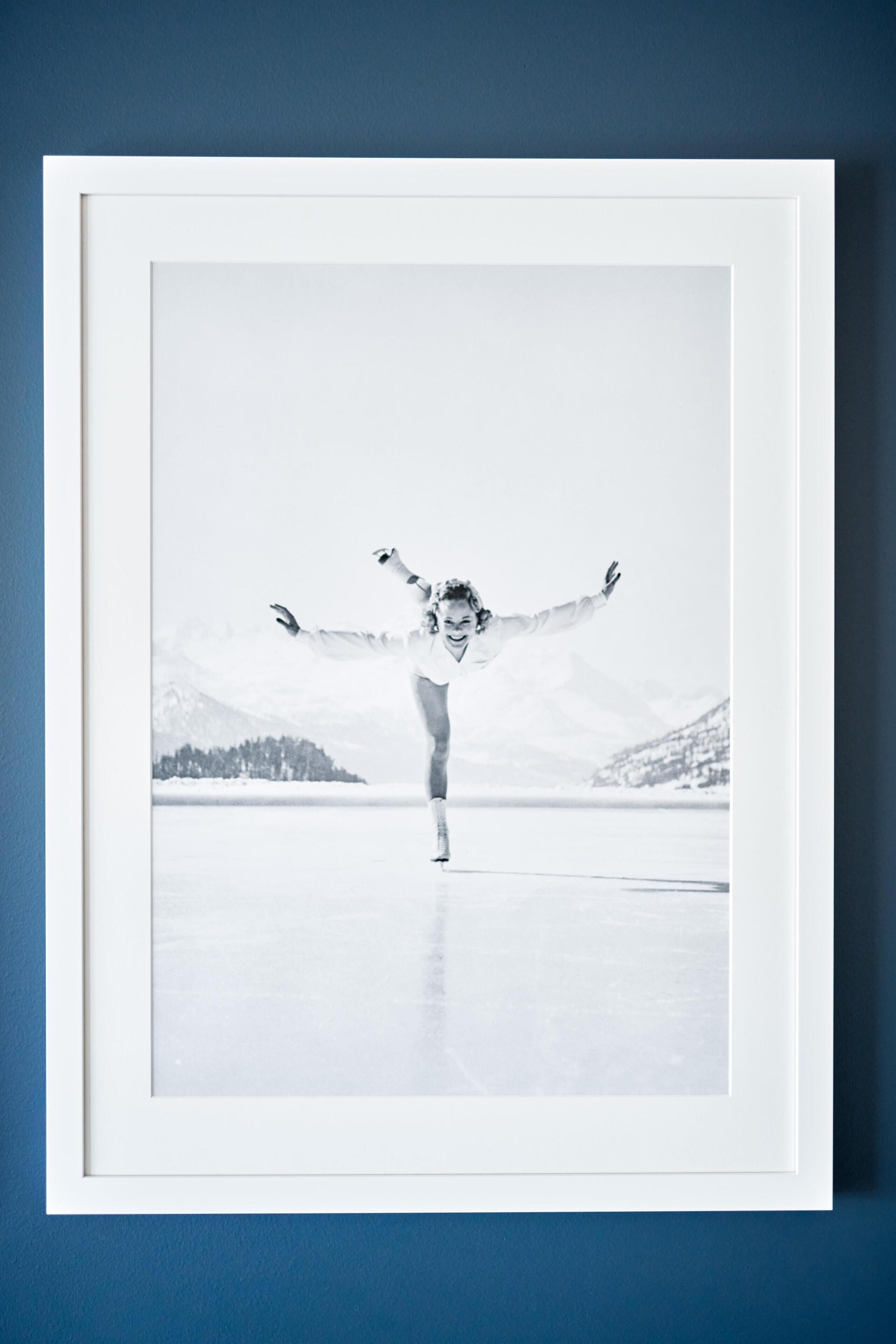 Een ingelijste foto van een persoon in een witte outfit op een reflecterend oppervlak, met een bergachtig landschap op de achtergrond.
