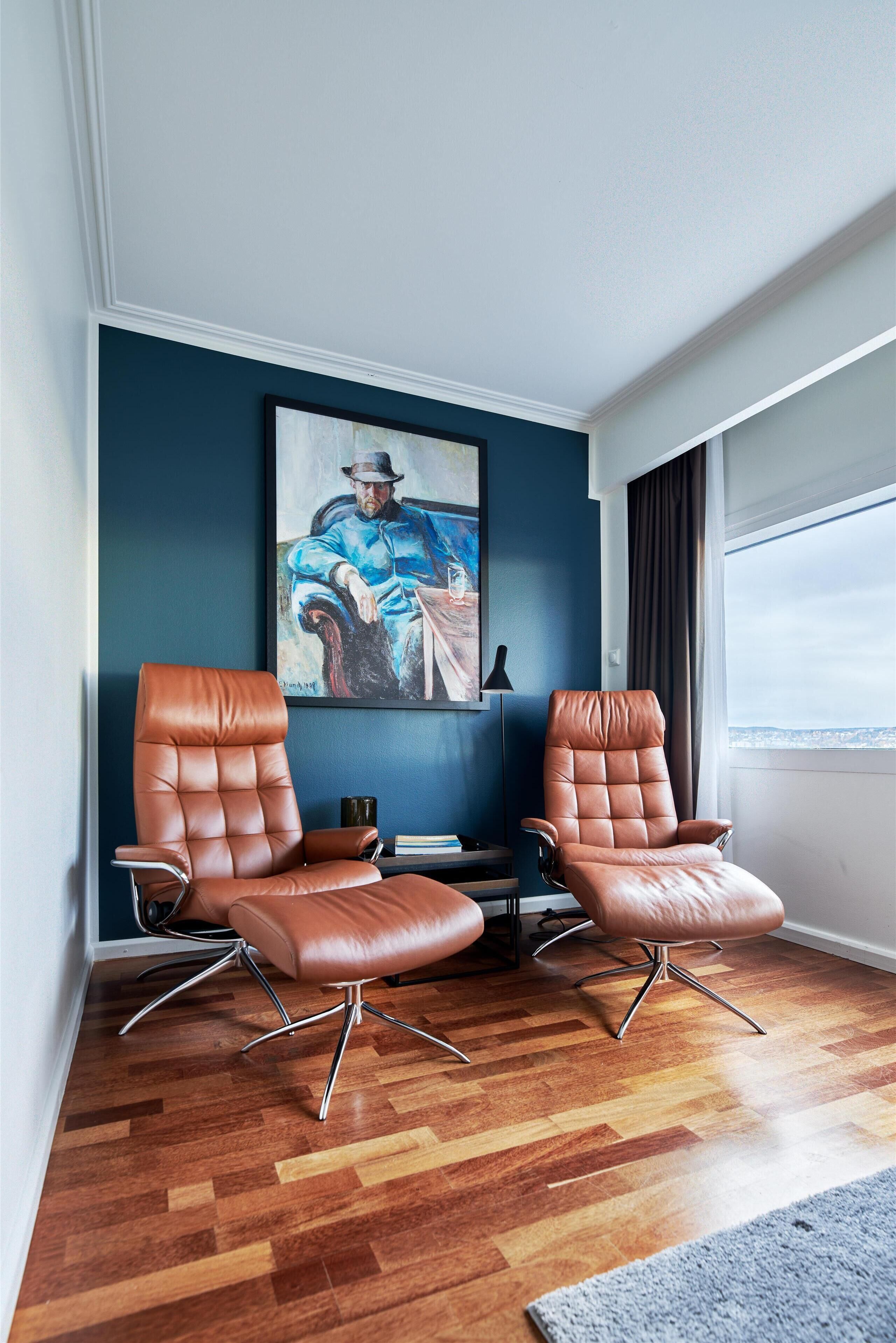A room with two leather armchairs, a painting on the wall, and a view through a window.