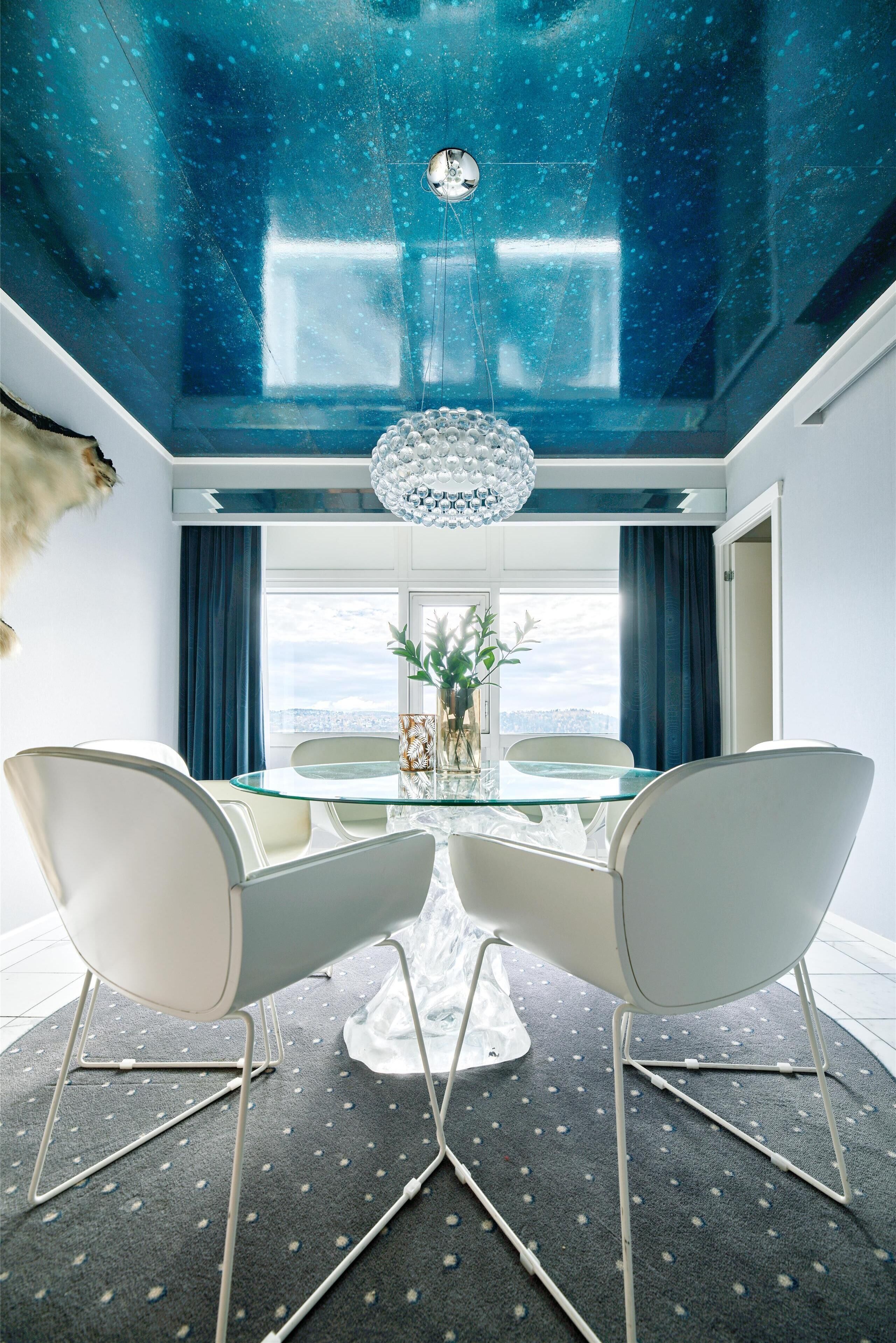 A modern dining room with a glass table, white chairs, and a chandelier.