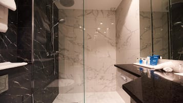 Un baño moderno con ducha de vidrio, azulejos de mármol y tocador con artículos de aseo.