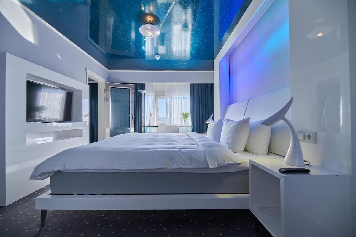 A modern bedroom with a bed, a TV, and a ceiling with a starry design.