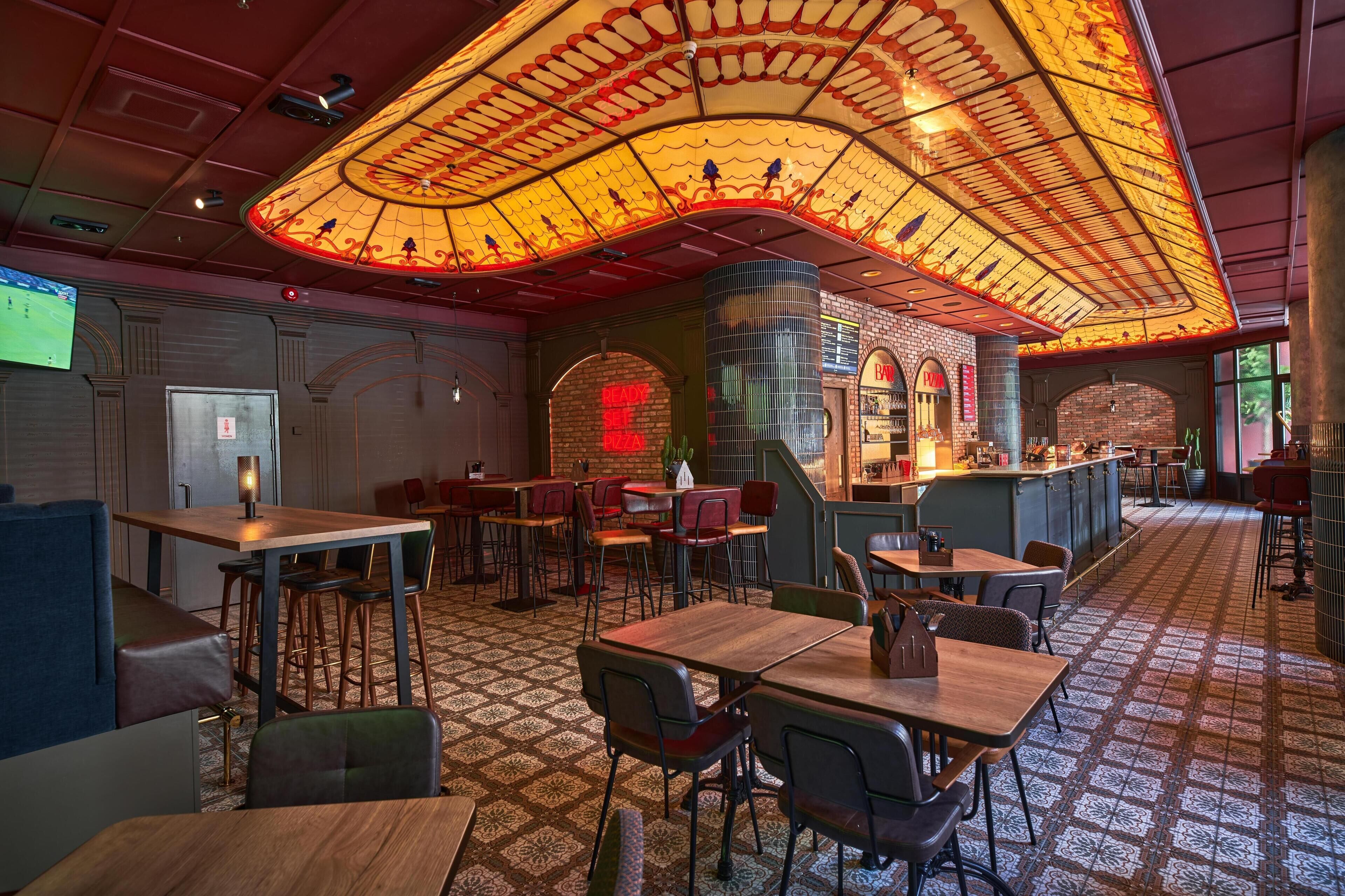 A restaurant with a patterned floor, wooden tables and chairs, and a distinctive ceiling design.